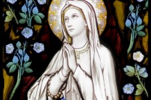 Catholic stained glass window showing the Virgin Mary surrounded by blue flowers